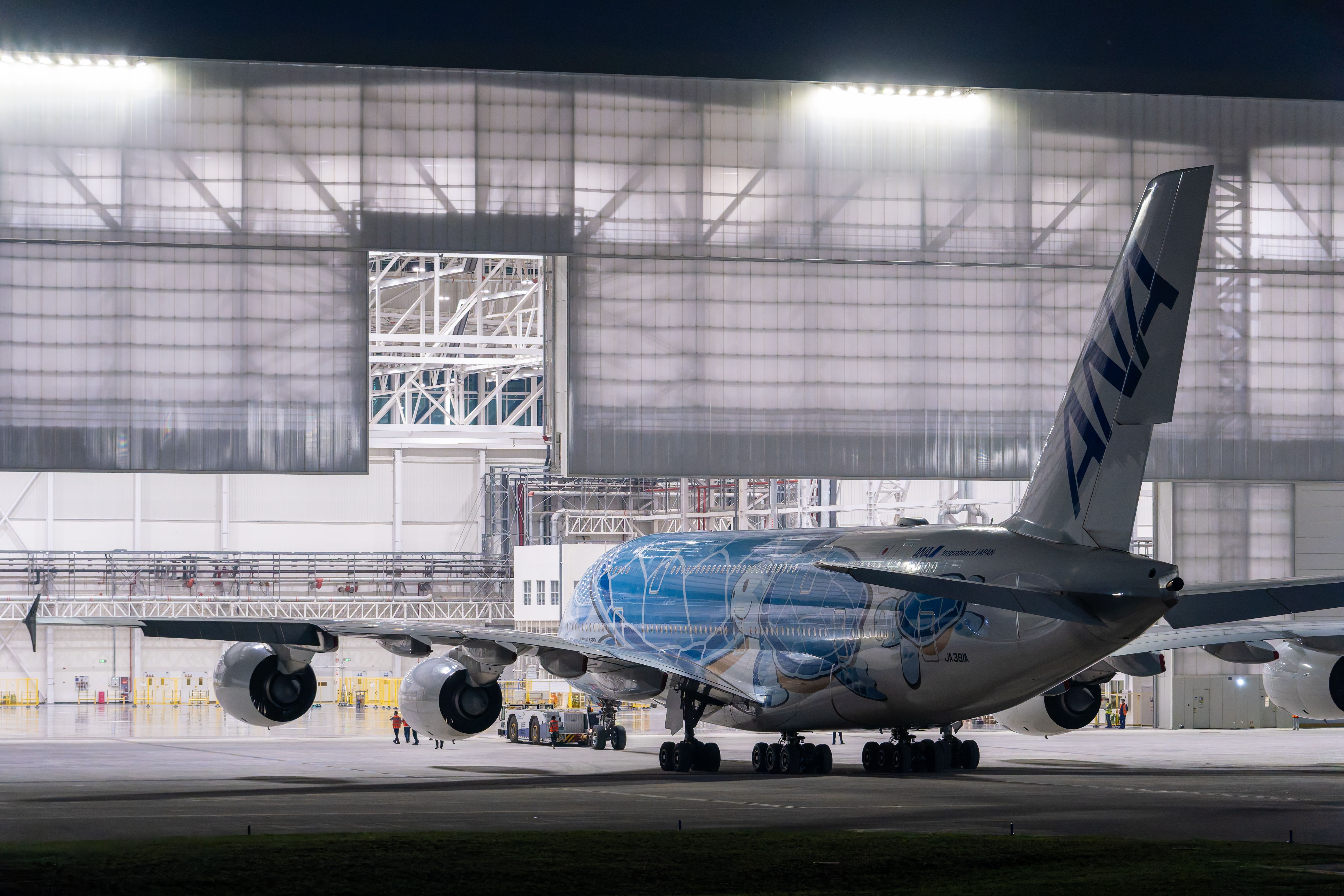 Wide-body aircraft inside an illuminated maintenance hangar at night